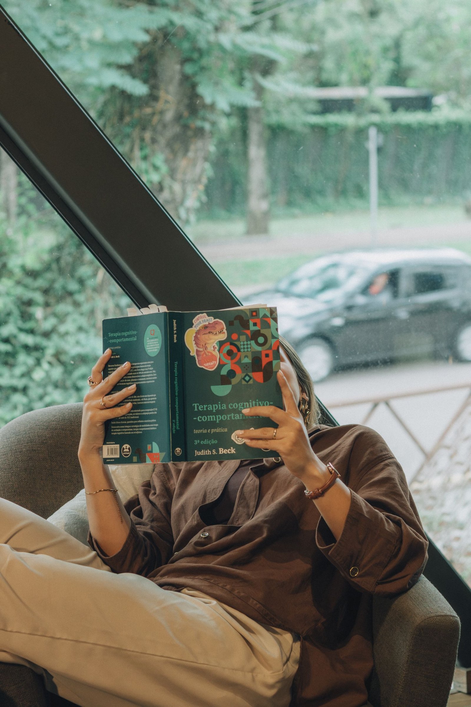 Woman reclining in a chair indoors, enjoying a book by the window.
